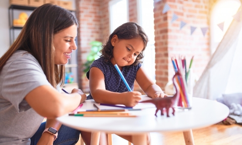 Beautiful teacher and toddler girl drawing draw using colored pencils at kindergarten