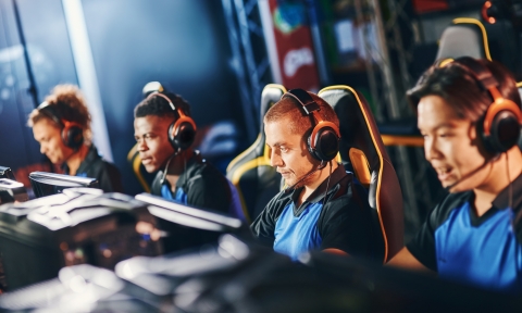Team of four professional cybersport gamers wearing headphones participating in eSport tournament, playing online video games