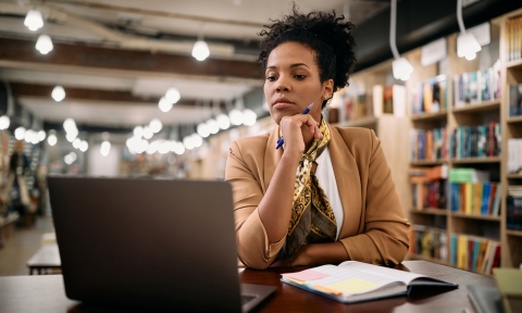 Mid adult black university professor working on laptop in a library.