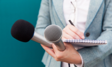 Female journalist at press conference, writing notes, holding microphone