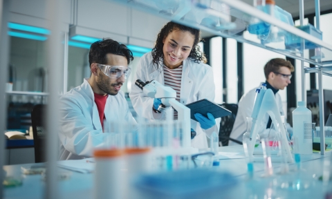 Grado Superior en Laboratorio Clínico y Biomédico Modern Medical Research Laboratory: Portrait of Latin and Black Young Scientists Using Microscope, Digital Tablet, Doing Sample Analysis, Talking. Diverse Team of Specialists work in Advanced Lab