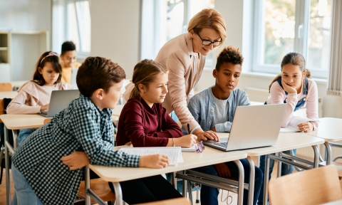 Group of elementary students having computer class with their teacher in the classroom.