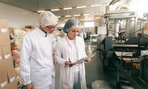 Doctorado en Industria Alimentaria Two quality professionals in white sterile uniforms checking quality of salt sticks while standing in food factory.
