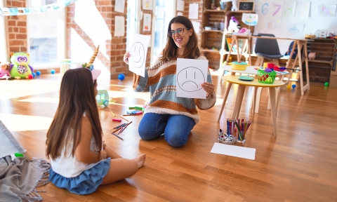 Doctorado de Pedagogía Beautiful pshychologist and toddler doing therapy with emotions emoji around lots of toys at kindergarten
