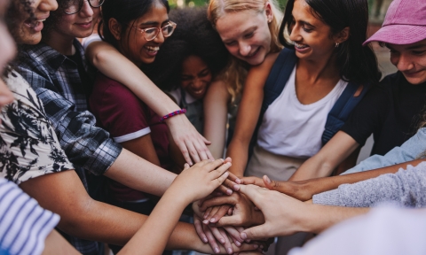 Cheerful teenagers putting their hands together in unity