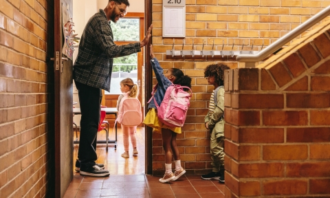 Grado de Enseñanza Primaria Elementary school teacher greeting his students at the door. Male teacher welcoming his class with a high five